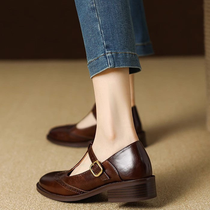 Close-up of the T-bar strap and brogue detailing on a women's beige Mary Jane shoe.