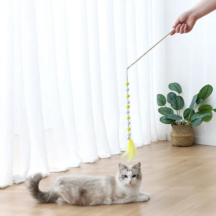 Cat pouncing on an interactive feather & pom pom play rod toy, perfect for pet enrichment.