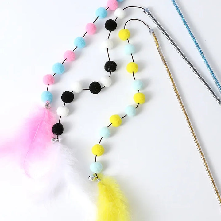 Kitten playing with a colorful feather & fuzzy pom pom interactive pet toy rod for playful cats.