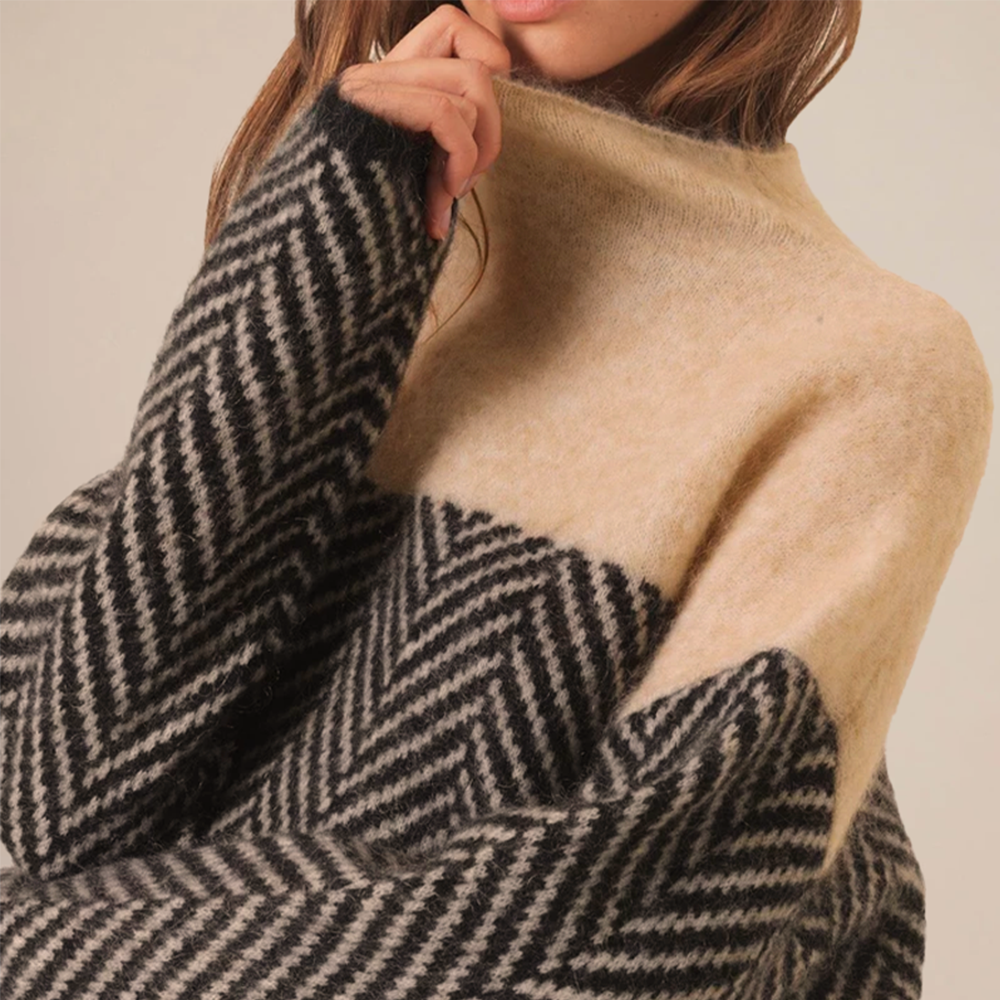 Close-up of the textured knit fabric on a women's high collar pullover sweater, emphasizing coziness.