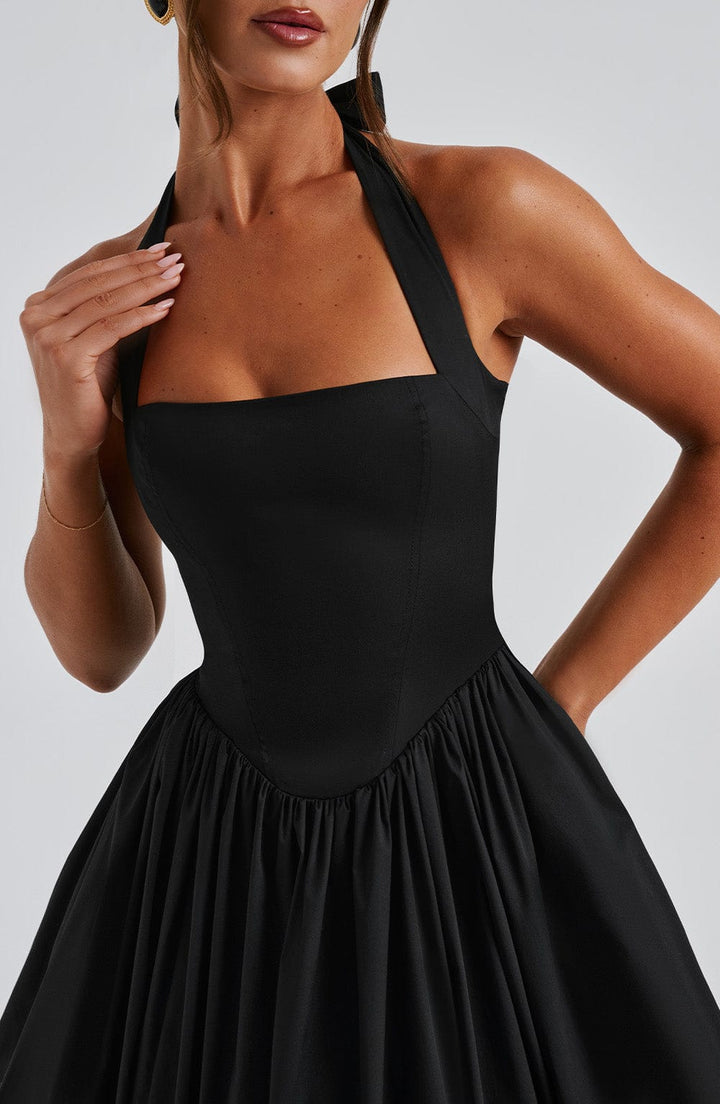 Full-body shot of a woman wearing a black halter neck wedding guest midi dress.