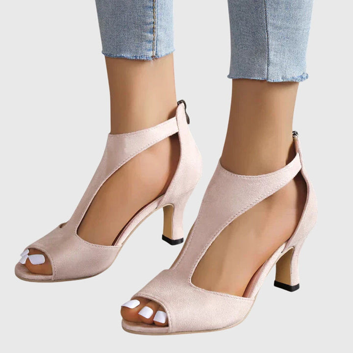 Close-up of the delicate straps and open toe design of women's pink stiletto heels, cutout detail.