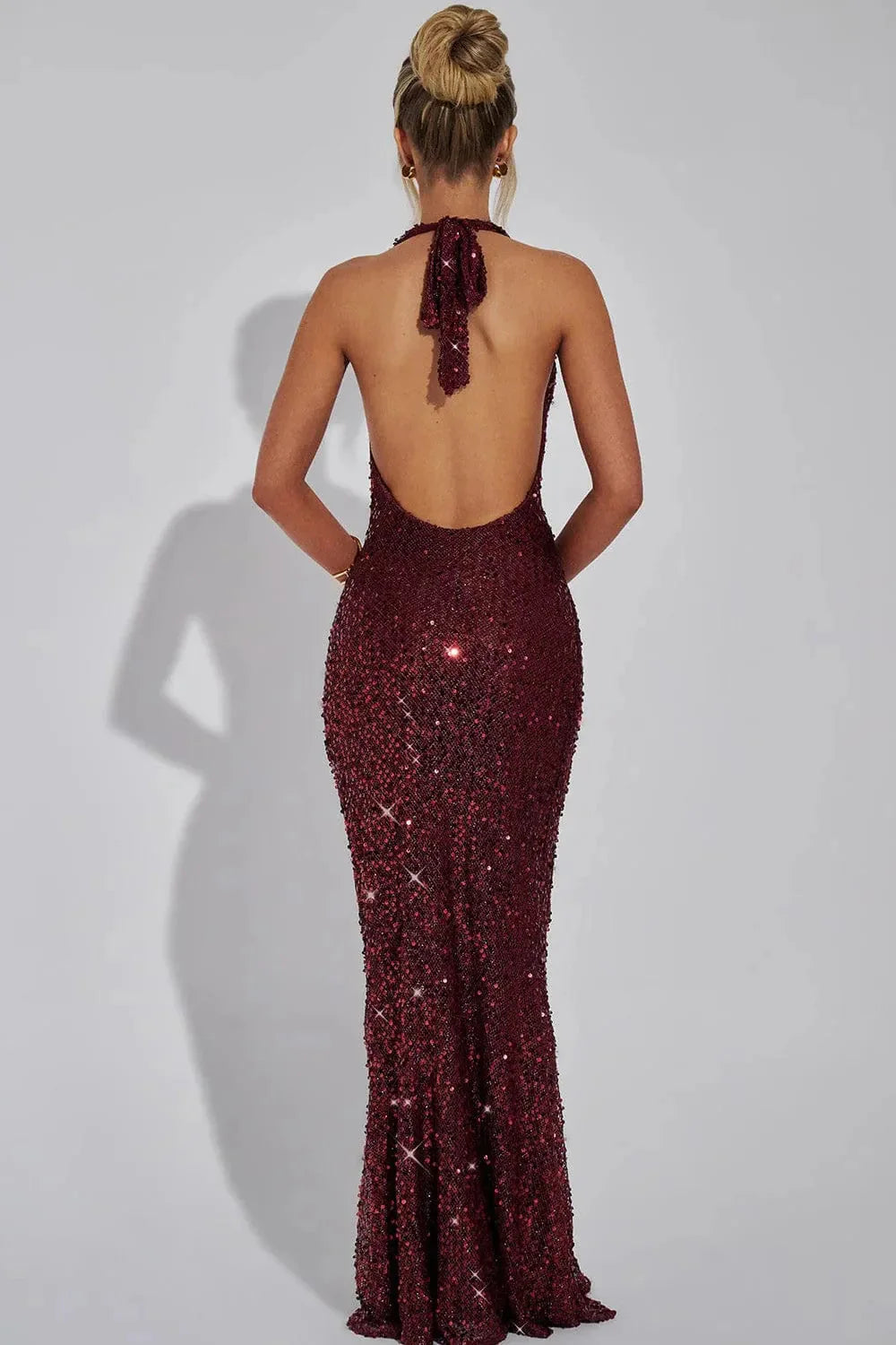 Close-up of women's sequin halter evening maxi dress, showing intricate sequin detail & open back design.