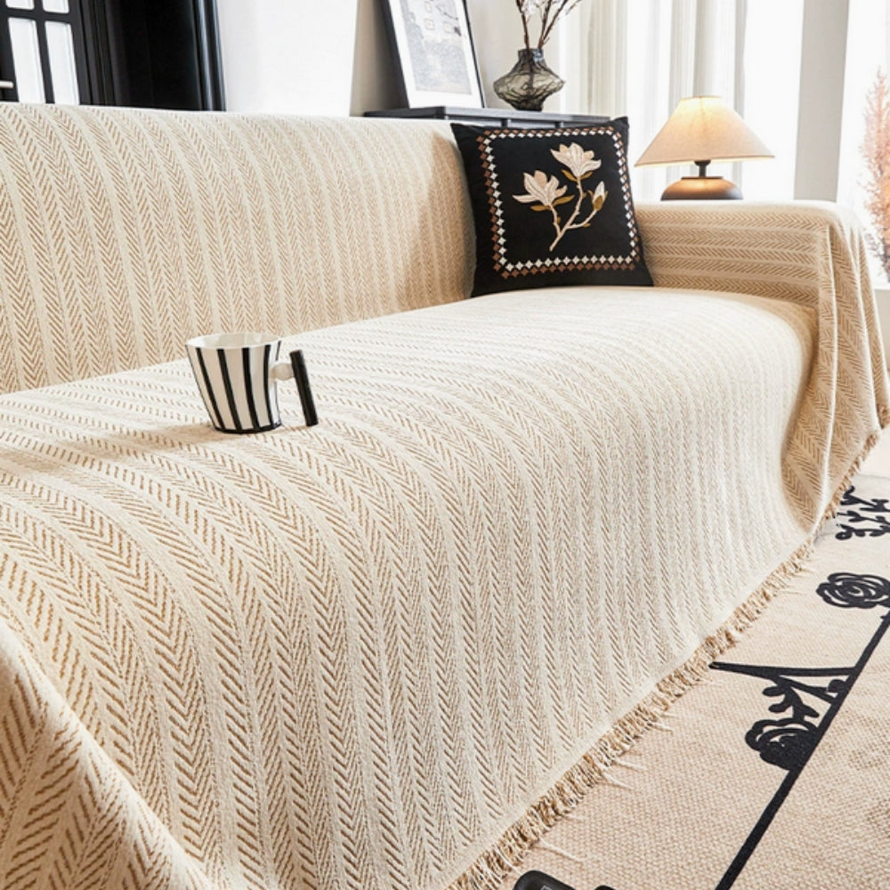 Herringbone chenille sofa cover with decorative tassels, protecting furniture in a living room.