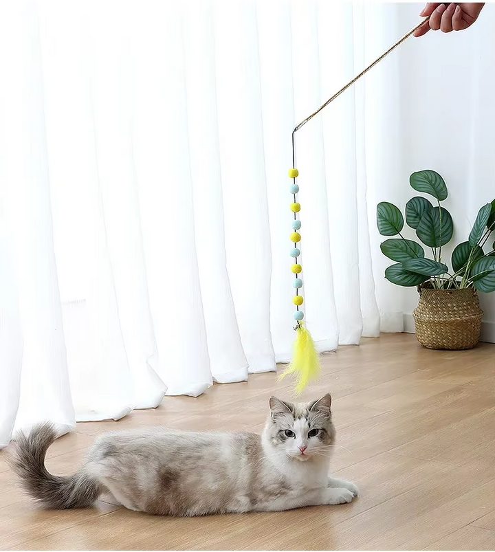 Close-up of interactive cat toy lure: colorful feathers & fluffy pom-poms on a flexible fishing rod.