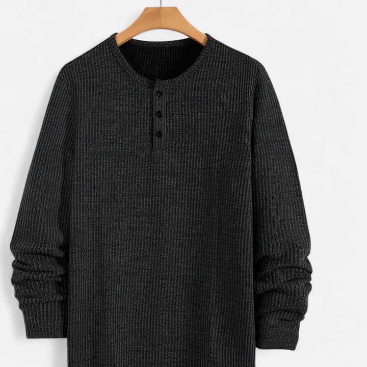 Detailed view of men's cable-knit henley sweater, long sleeve, showing intricate knit pattern & button front.