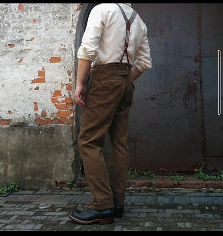 Detailed view of men's elegant brown pleated dress pants with classic front pleats and adjustable suspenders.