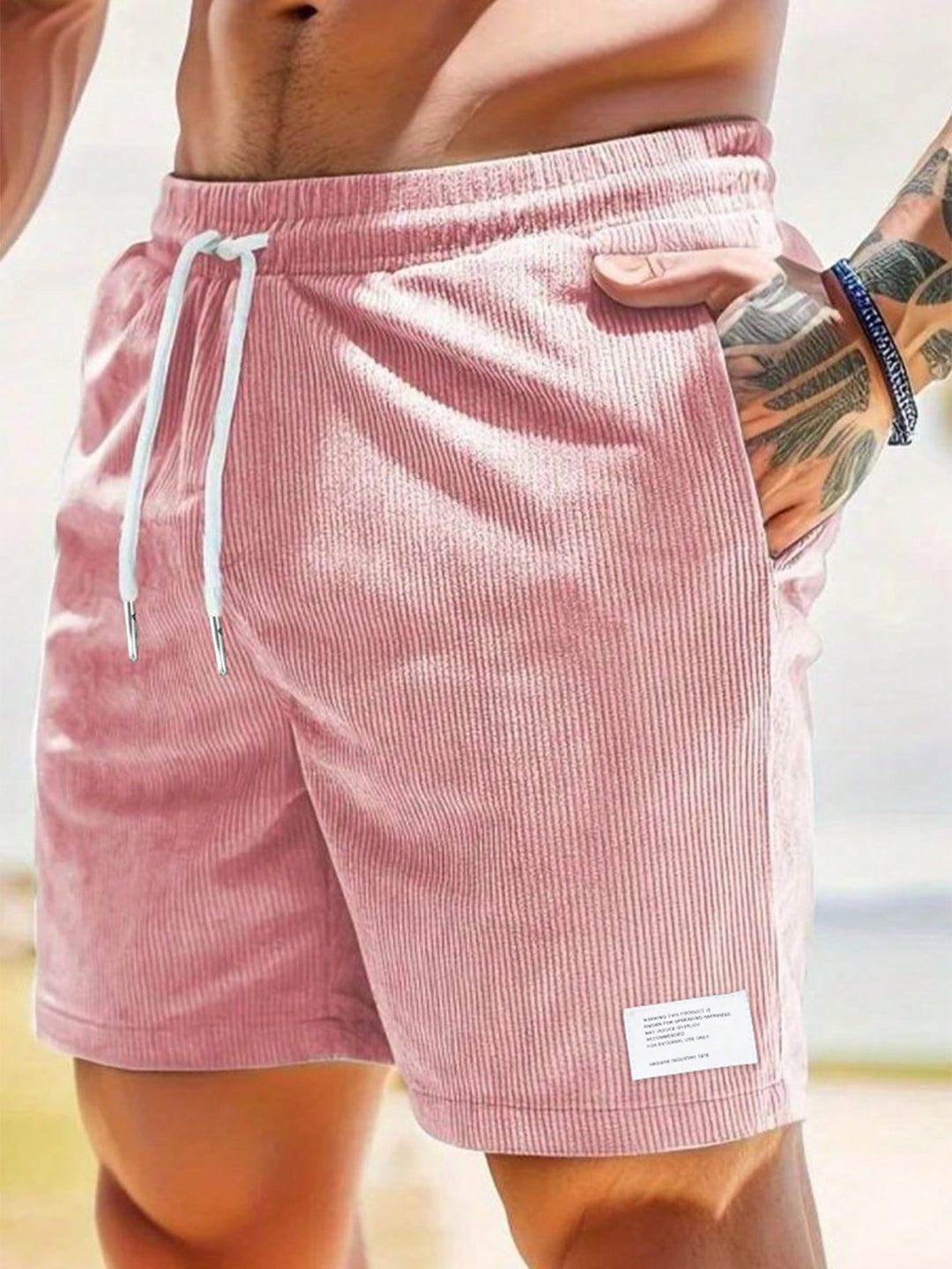 A pair of men's relaxed fit drawstring shorts on a sandy beach, hinting at beachwear and summer lifestyle.