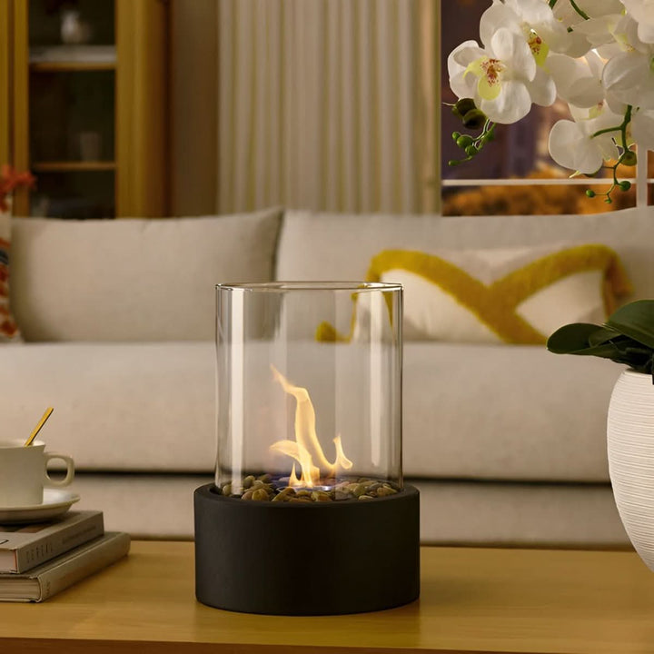 Bioethanol table fireplace featuring a clear glass cylinder and durable metal base. Ambiance lighting.