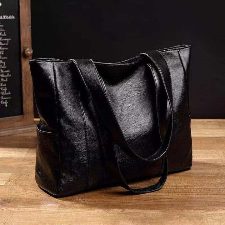 Spacious black faux leather women's everyday tote bag with comfortable shoulder straps & large pockets, for work or travel.