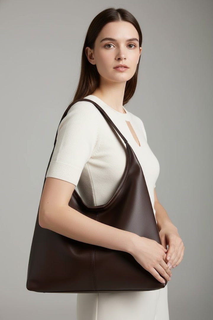 Woman's hand holding the sturdy strap of a black faux leather classic tote bag, ready for everyday use.