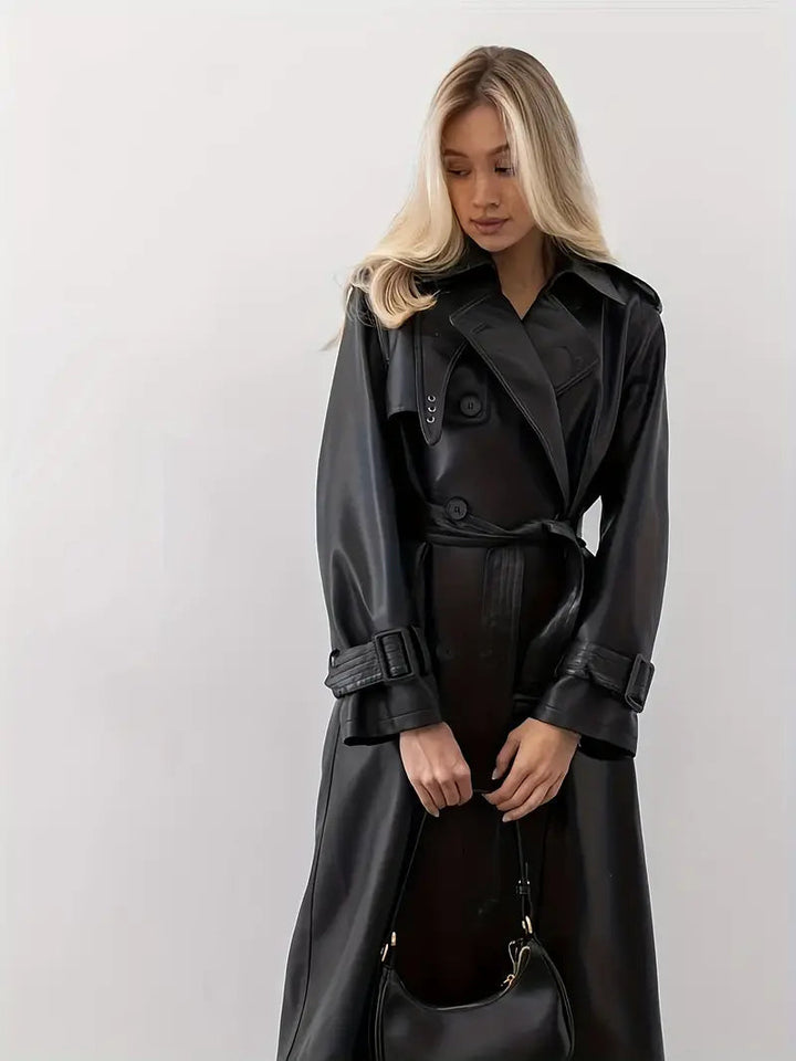 Fashionable women's black faux leather trench coat with double-breasted design and belt.