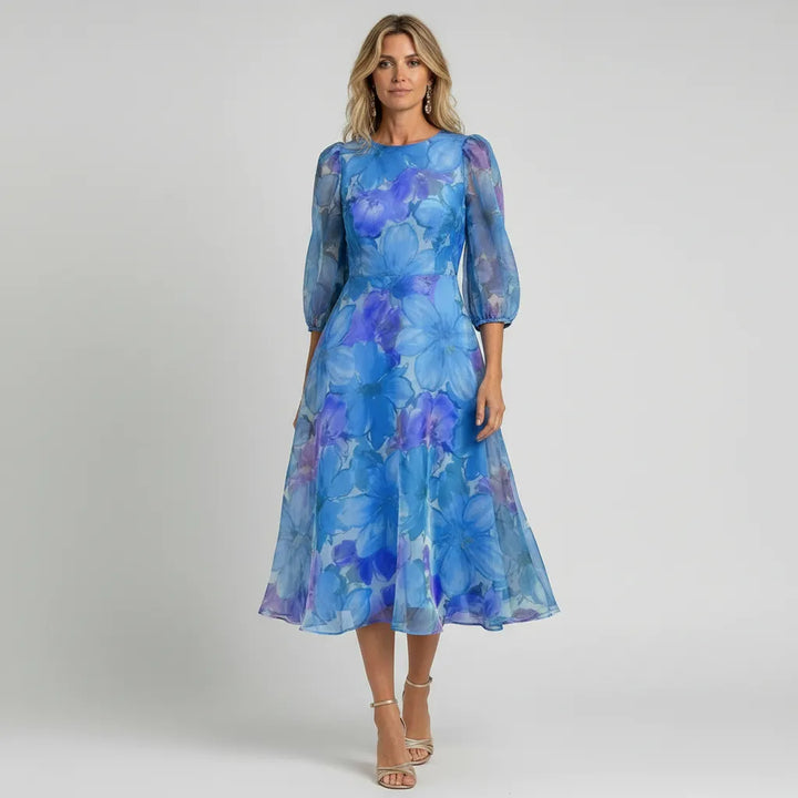 Blue floral sheer midi dress with puff sleeves. Chic summer fashion, ideal for women's elegant outdoor events.