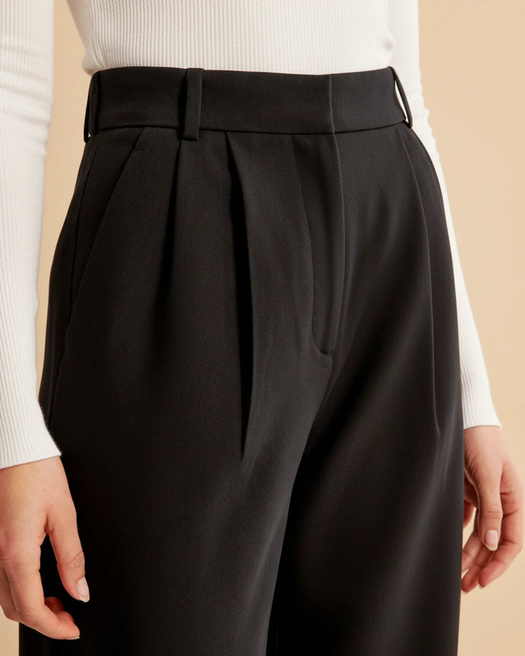 Detail of the high waist and button closure on women's tailored pleated trousers, an officewear essential.