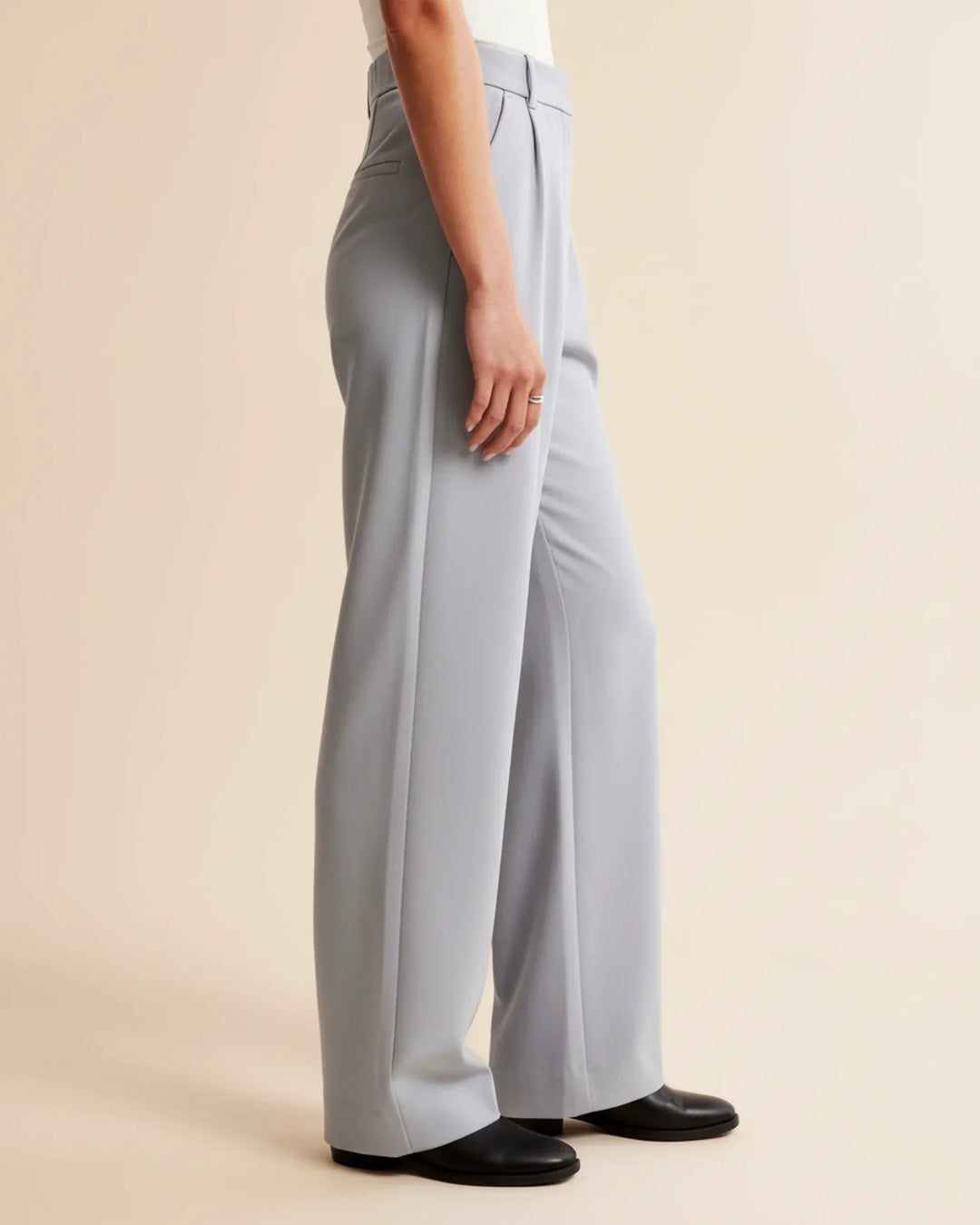 Model walking in women's high-waisted pleated tailored trousers, illustrating their movement and comfort.