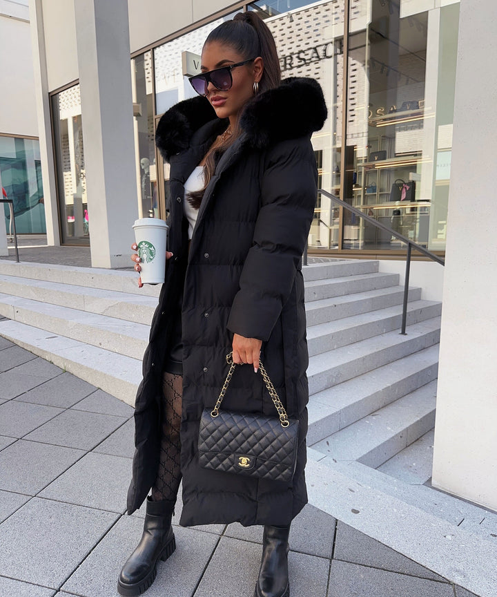 Side profile of a women's long quilted hooded jacket, with a cinched waist belt for a chic look.