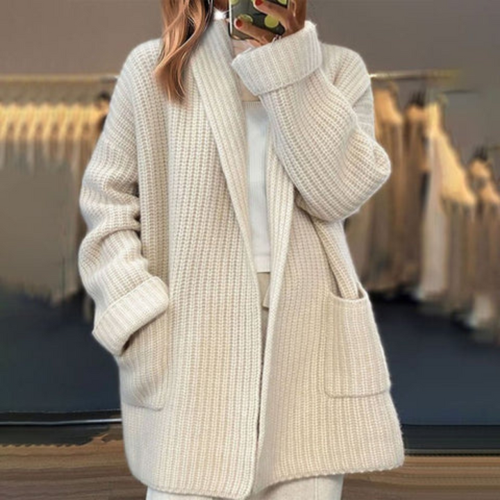Close-up of a women's beige knit oversized cardigan, showing wool texture and practical front pockets.